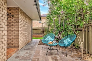 A patio with two blue chairs, a small table, and a brick wall. - Hahndorf Creek Retreat 2 Bedroom (Hahndorf)