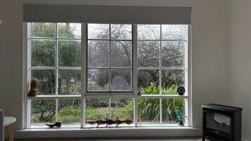A room with a large window, a small black stove, and a wooden shoe rack.