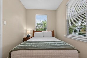 A bedroom with a bed, a nightstand, a lamp, and a window with blinds. - 6BR Central AUS w/ Fenced Yard + Pets, Fire pit! (Austin)