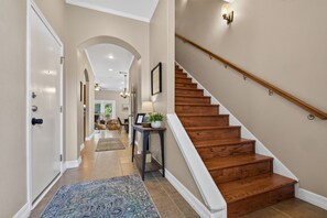 A hallway with a wooden staircase, a rug, and a door leading to a living area. - 6BR Central AUS w/ Fenced Yard + Pets, Fire pit! (Austin)