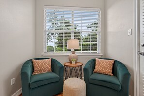 A room with two teal armchairs, a small round table with a lamp, and a window with blinds. - 6BR Central AUS w/ Fenced Yard + Pets, Fire pit! (Austin)