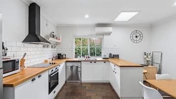 A modern kitchen with white cabinetry, a black range hood, a built-in dishwasher, and a window with a view of greenery.