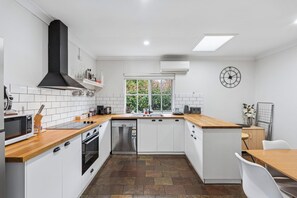 Una cocina moderna con armarios blancos, extractor de aire negro, lavavajillas integrado y ventana con vistas a zonas verdes.