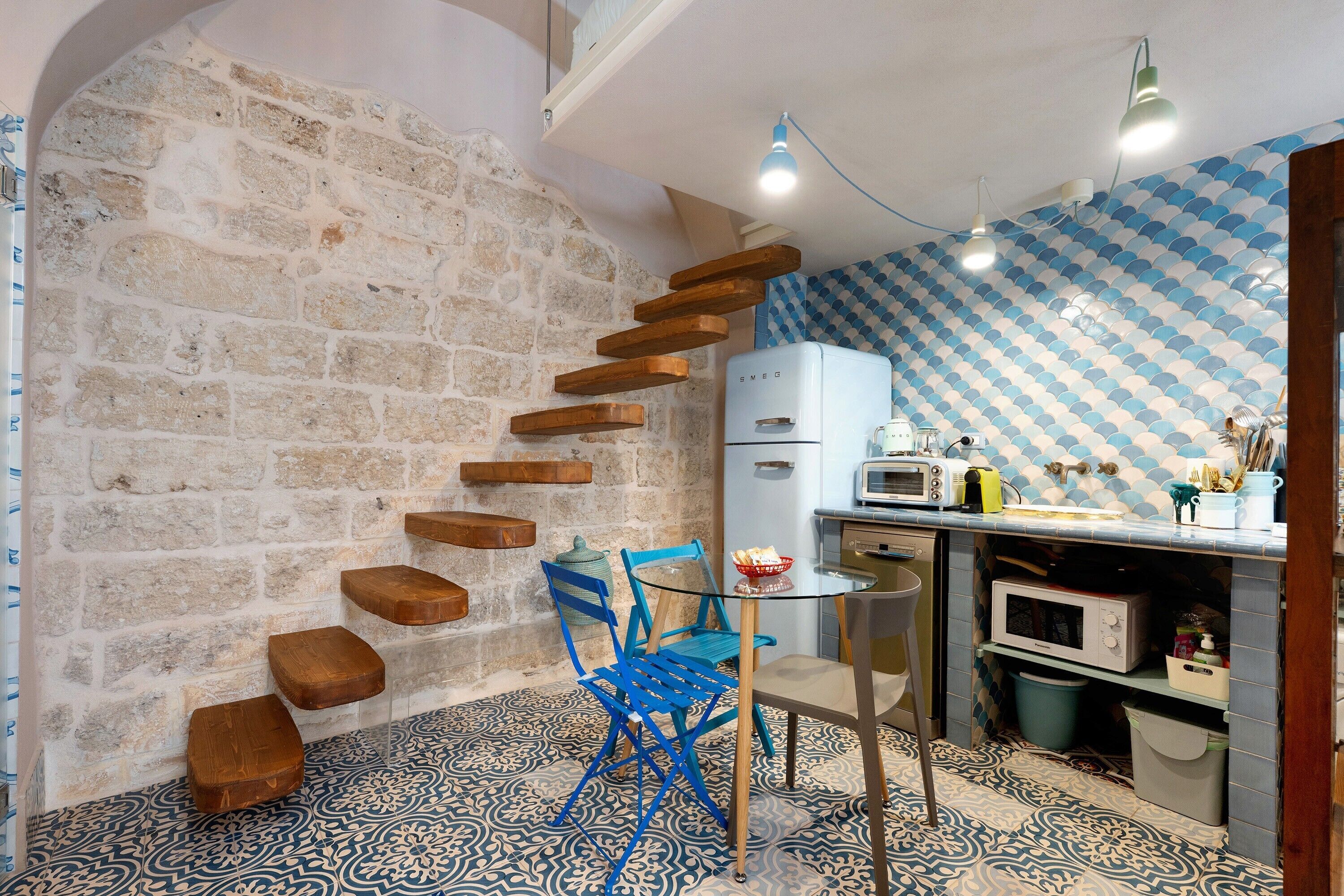 A kitchen with a stone wall, wooden steps, a blue chair, and a microwave.