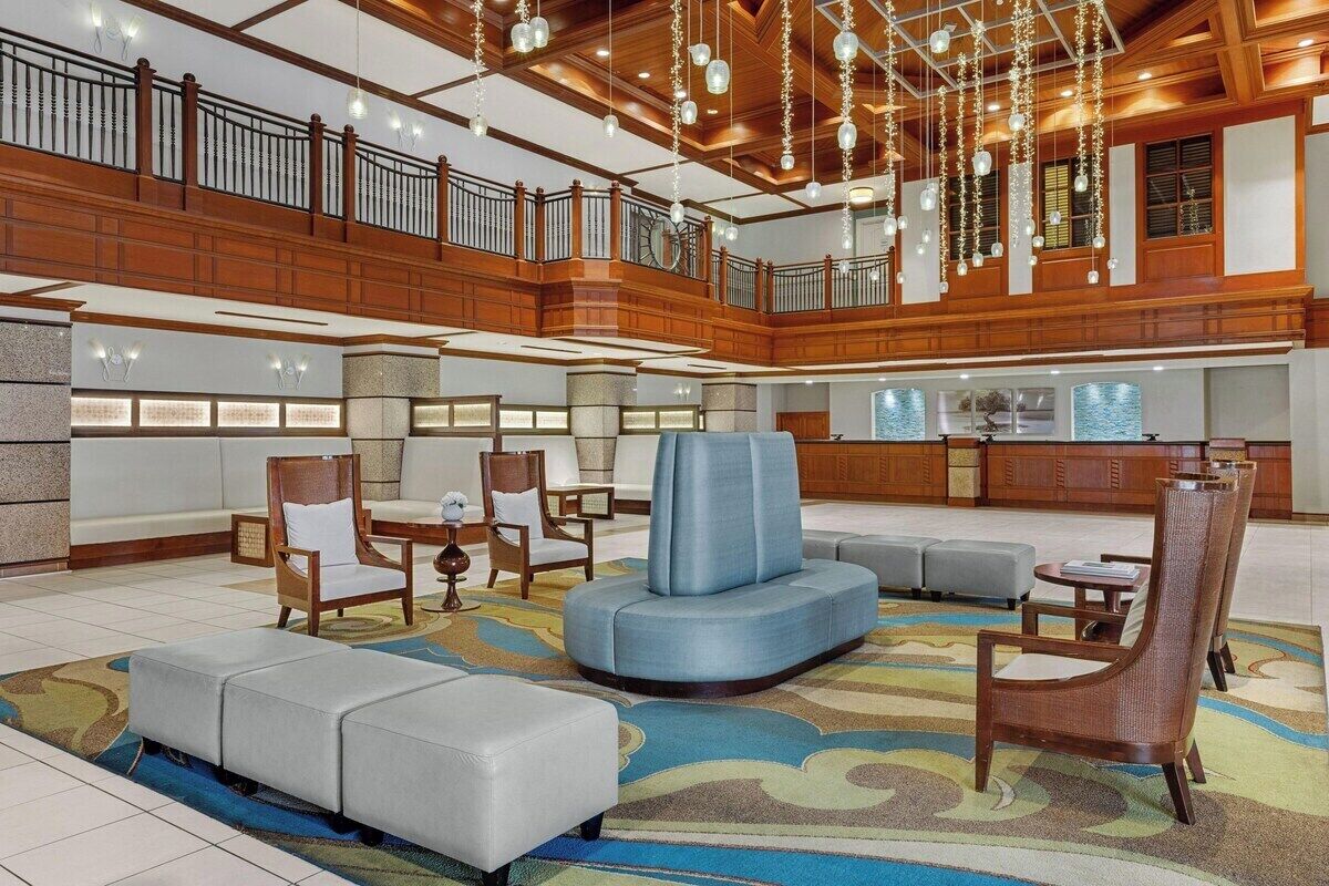 Een ruime lobby met een hoge plafond, houten lambrisering en een centraal zithoek met banken en stoelen.