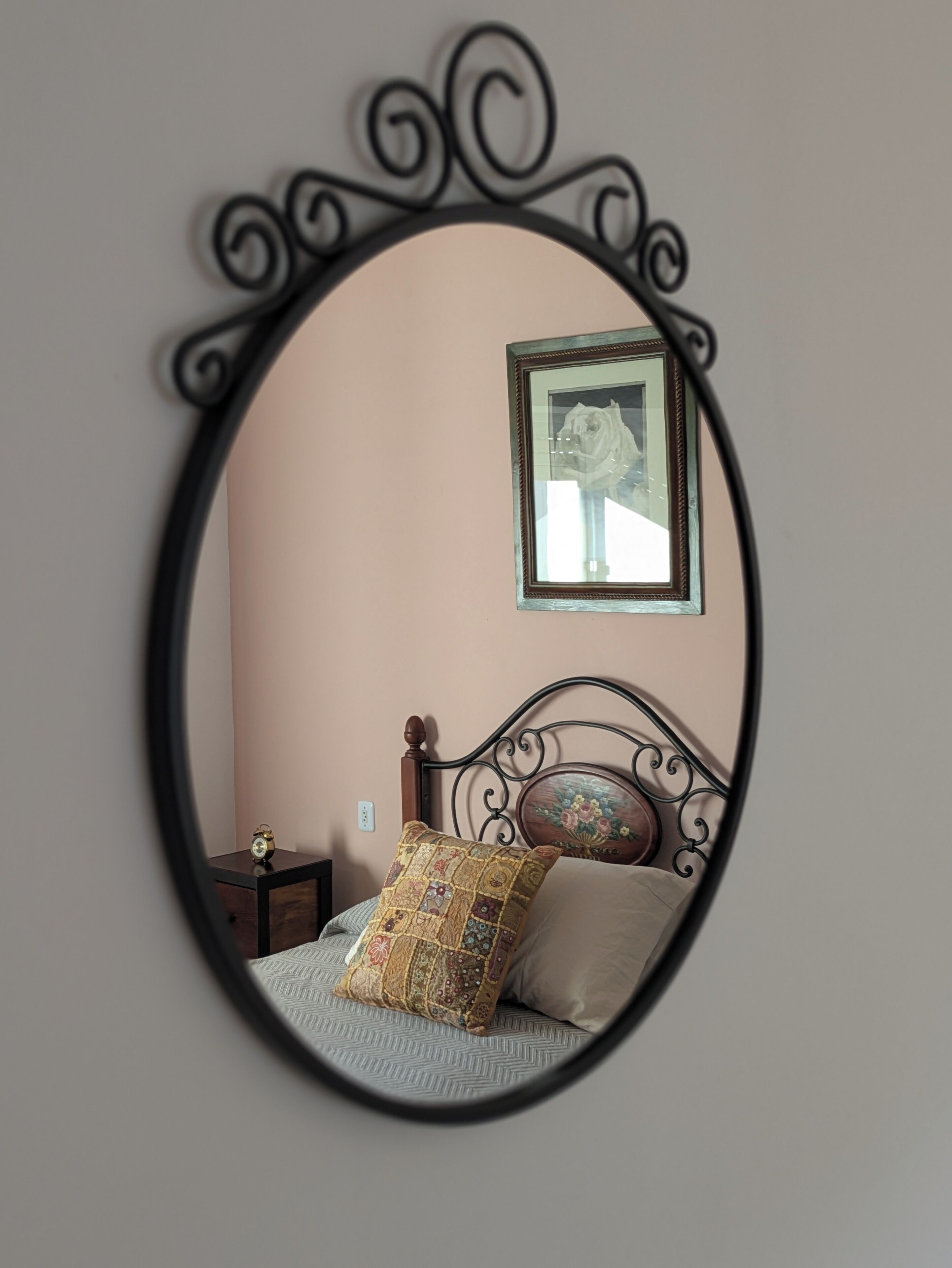 Un dormitorio con cama, mesita de noche, espejo y un cuadro colgado en la pared.