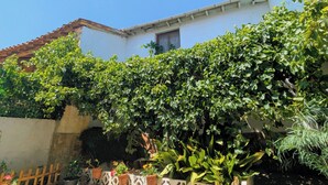 Um edifício com fachada branca, telhado telhado e área de jardim com diversas plantas e uma cerca decorativa.