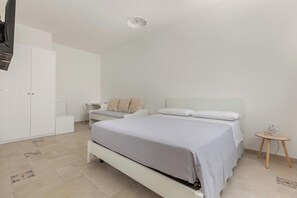 A minimalist bedroom with a bed, bedside tables, a wardrobe, and a small round table with a decorative item. - B&B Li Peticurti | Camera tripla (Santa Cesarea Terme)