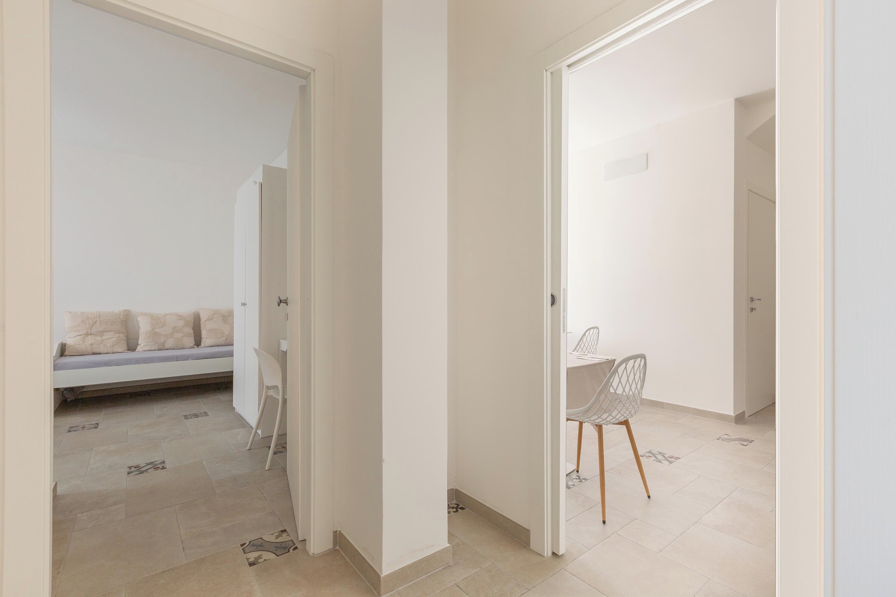 Ein Flur mit Sofa und Sessel, der zu einem Zimmer mit Bett führt.