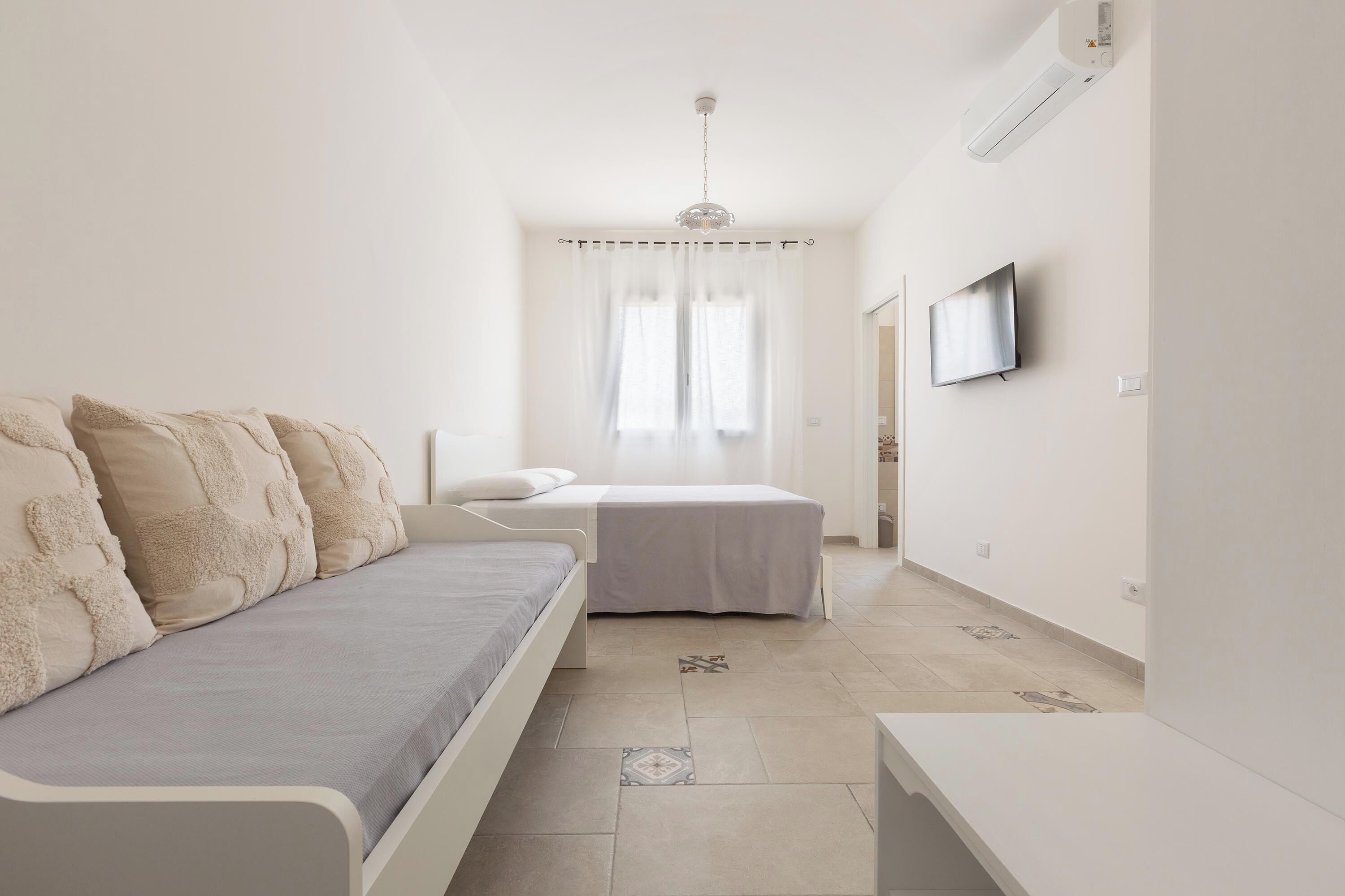 Una camera da letto minimalista con un letto, un divano, una TV e una ventola a soffitto.