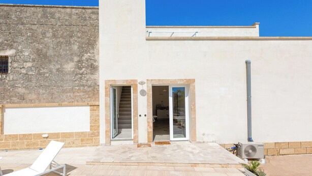 A building with a stone facade, a white exterior, and a clear blue sky. - B&B Li Peticurti | Camera tripla (Santa Cesarea Terme)