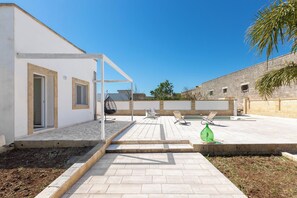 A modern outdoor patio with a pool, seating area, and a white building with a pergola.