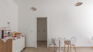 A modern kitchen with a dining area, featuring a white table, chairs, and a countertop with food items. - B&B Li Peticurti | Camera tripla (Santa Cesarea Terme)