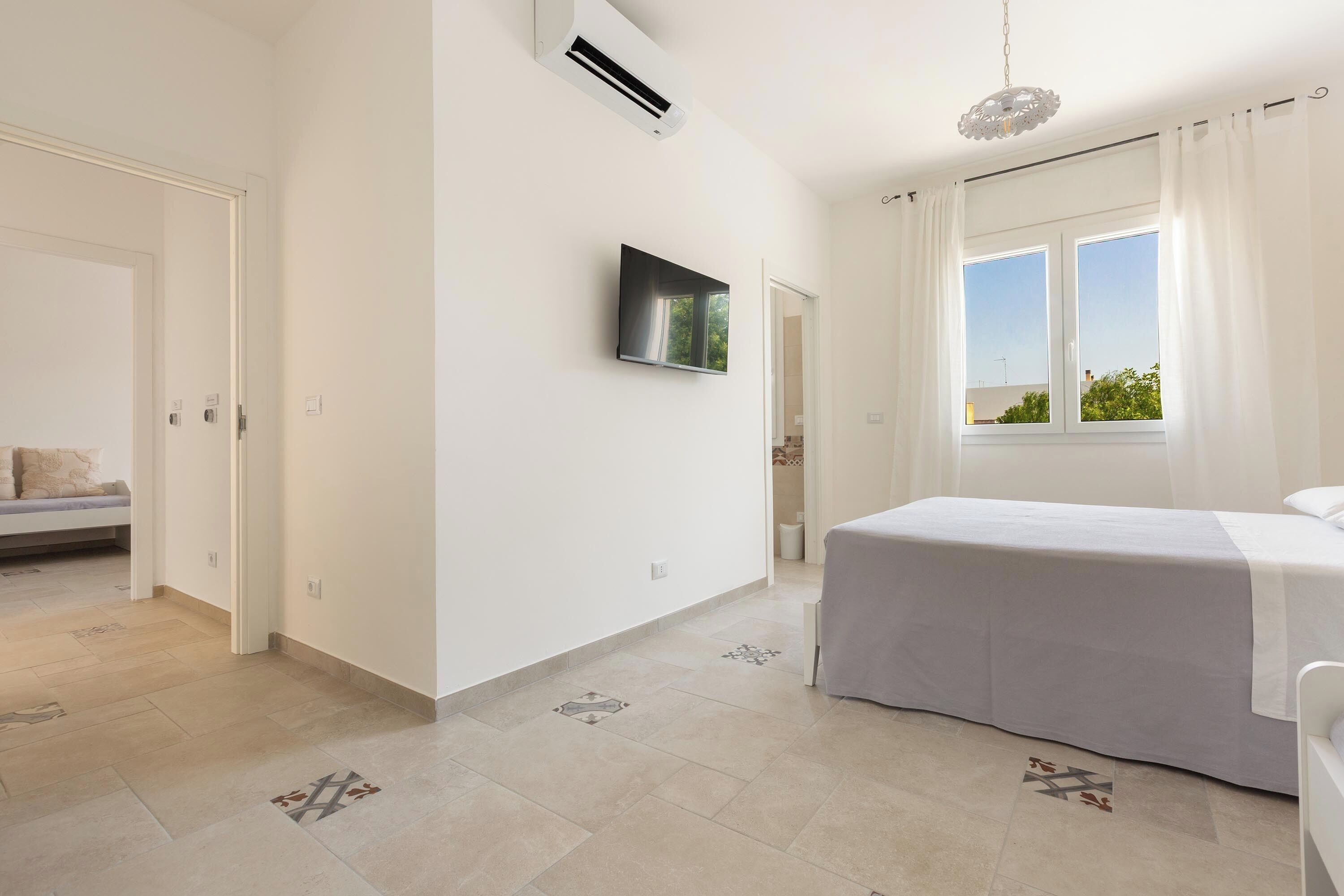 Un dormitorio con una cama, un televisor montado en la pared y una ventana con cortinas.
