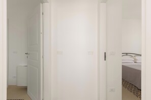 Ein schmaler Flur, der zu einem Zimmer mit einem Bett, einem Heizkörper und einer Tür führt.