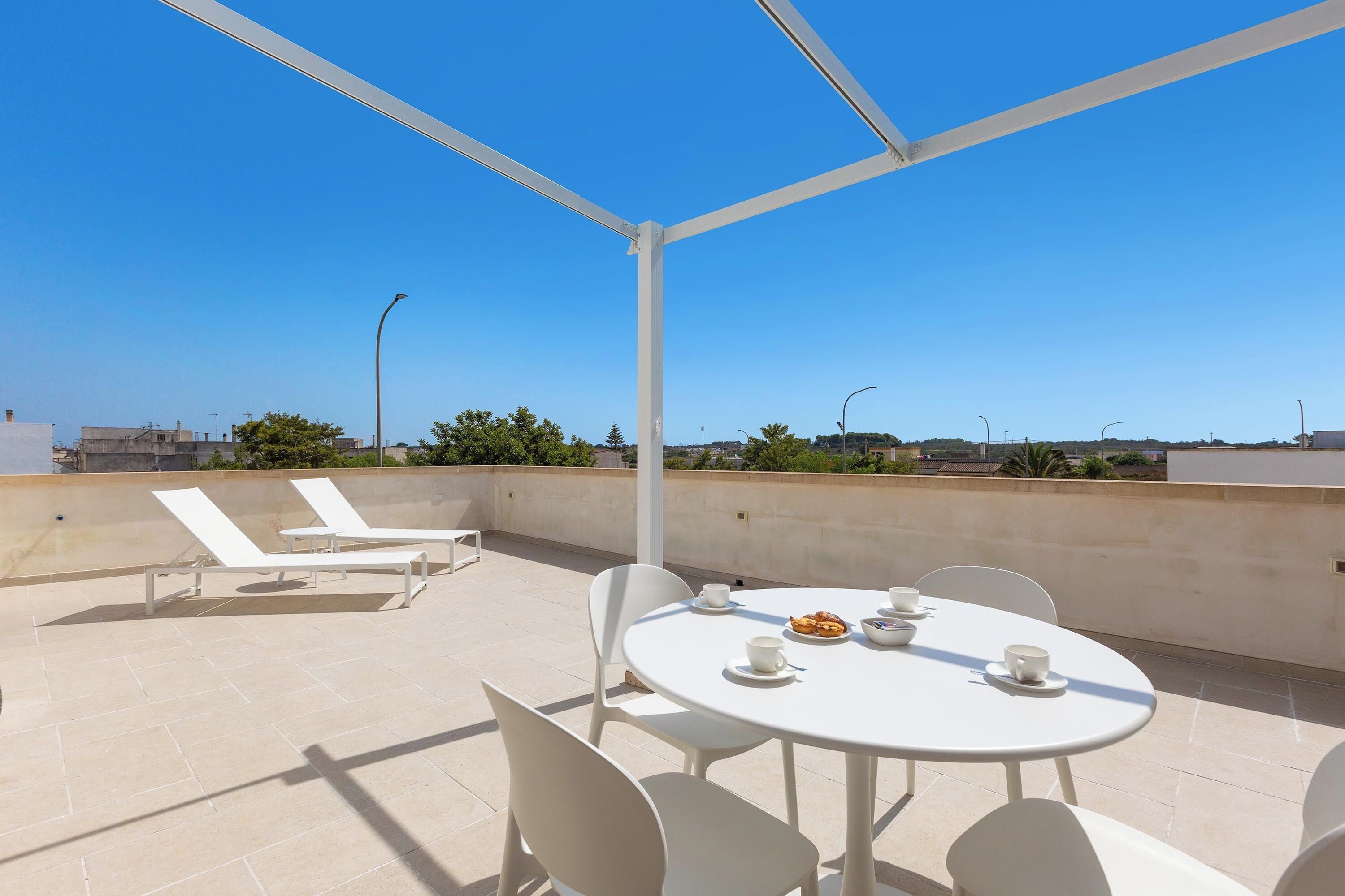 A rooftop terrace with a round table, white chairs, and lounge chairs.