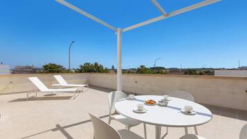 Una terrazza panoramica con un tavolo rotondo, sedie bianche e poltrone da relax.