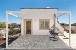 A white building with a patio area, a hanging chair, and a view of the street. - B&B Li Peticurti | Camera quadrupla (Santa Cesarea Terme)