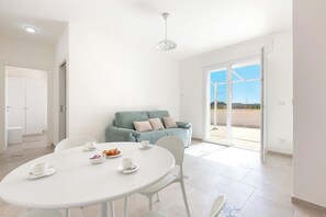 A modern living room with a round dining table, a sofa, and a large sliding glass door leading to an outdoor area.