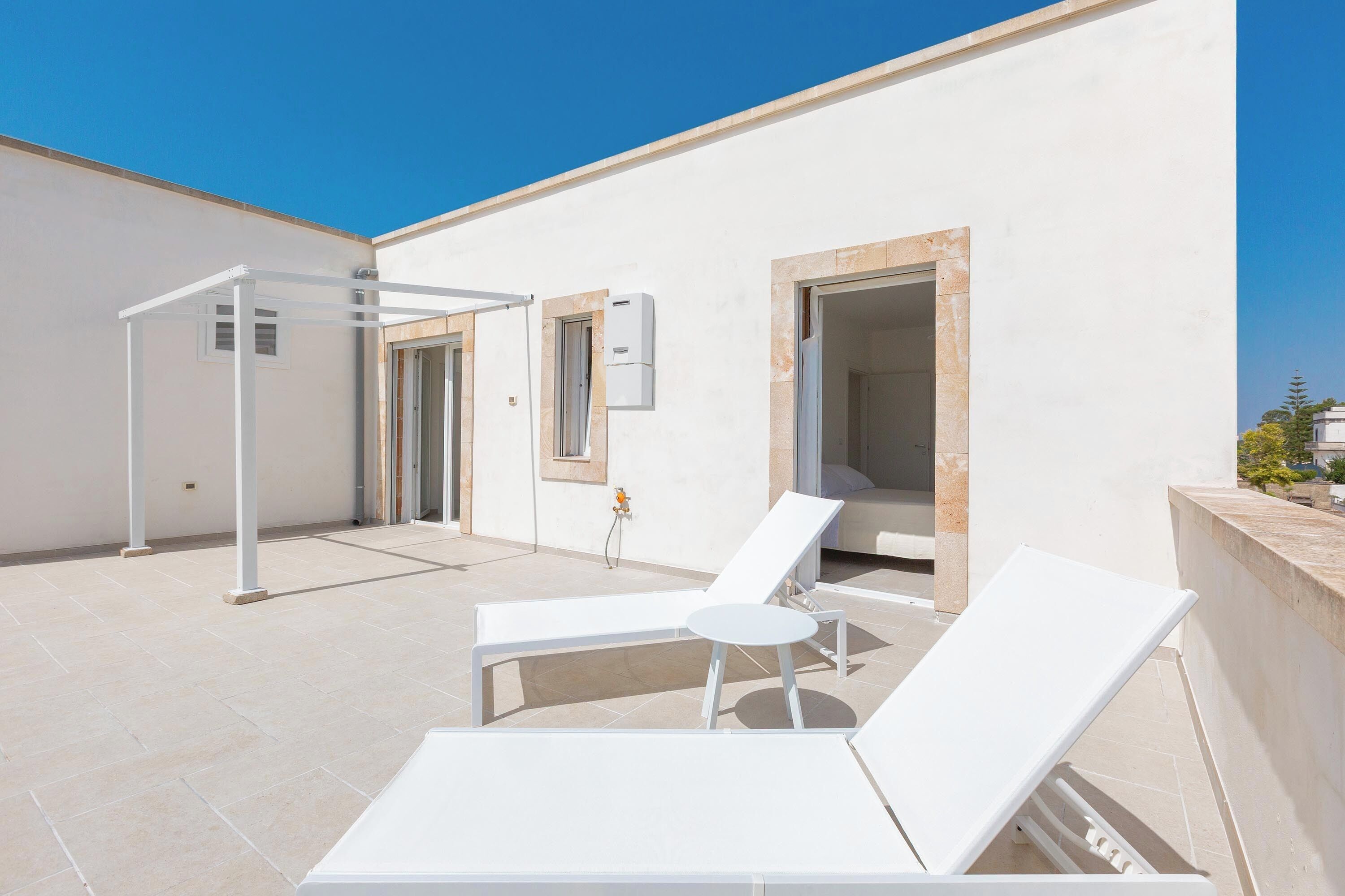 Una terrazza sul tetto con poltrone da relax bianche, un pergolato e una fontana.