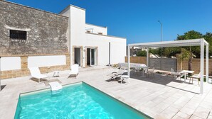 Piscina com espreguiçadeiras e área de estar coberta.