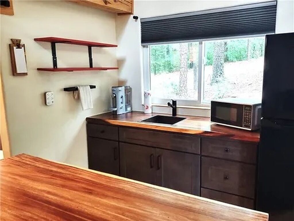 A kitchen with a wooden countertop, a microwave, a sink, and a window with a view of greenery.