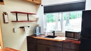 Una cucina con un piano di lavoro in legno, un forno a microonde, un lavello e una finestra con vista su spazi verdi.