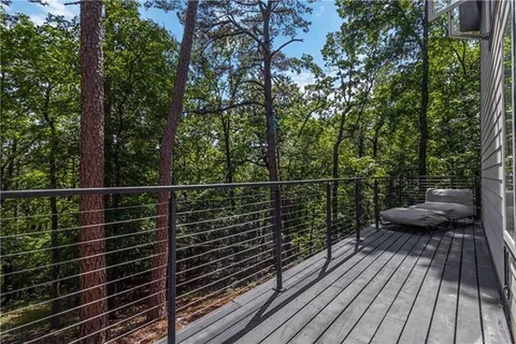A deck with a metal railing, surrounded by trees, and a sofa with cushions.