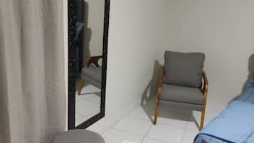 Um quarto com uma cama, uma cadeira, um banquinho e um espelho.