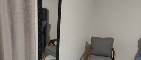 A bedroom with a bed, a chair, a small stool, and a mirror.