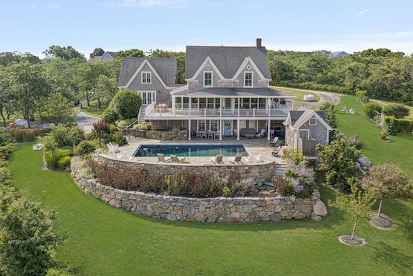 A large house with a pool, surrounded by a well-maintained lawn and stone walls.