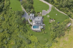 A large house with a swimming pool, surrounded by lush greenery and a well-maintained lawn.
