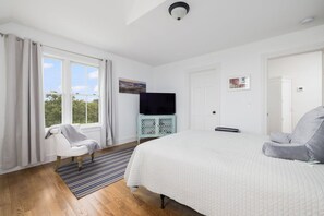 A bedroom with a large bed, a television on a cabinet, a chair, and a view of the outdoors.