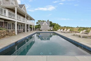 A swimming pool with a covered deck area, lounge chairs, and a stone wall. - Sea House with Heated Pool (New Shoreham)