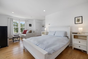 A bedroom with a large bed, a desk, and a chair. There is a window with curtains, a door, and a wall-mounted picture.