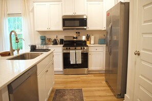 A kitchen with white cabinets, stainless steel appliances, a coffee maker, and a dish rack. - Boho Coastal Retreat - Bay + 30A Beaches - Tesla Charger - Sleeps 7 (Santa Rosa Beach)