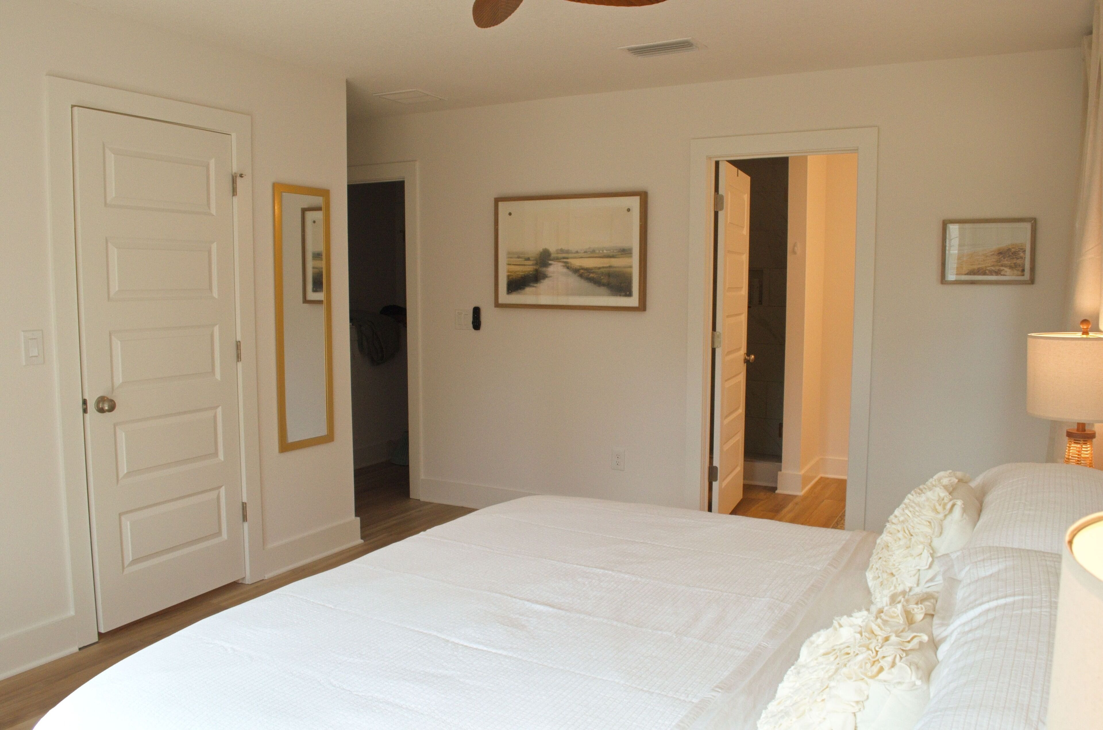 A bedroom with a bed, a door, a hallway, and a painting on the wall.