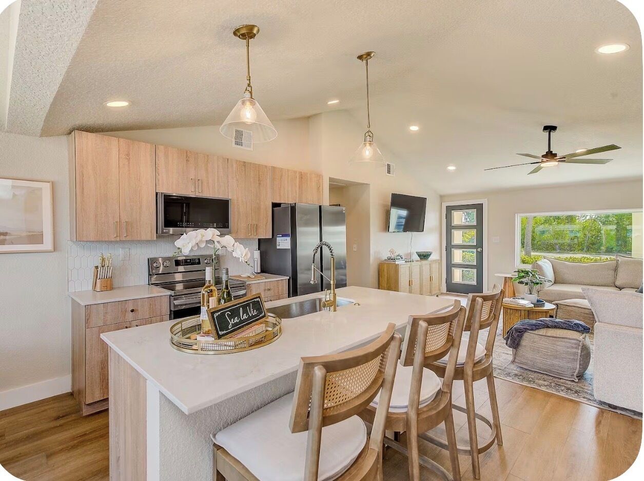 A modern kitchen with a large island, wooden cabinets, stainless steel appliances, and pendant lighting.