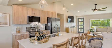 Una cocina moderna con una isla grande, armarios de madera, electrodomésticos de acero inoxidable e iluminación colgante.