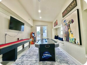 Une pièce équipée d’une table de billard, d’un baby-foot, d’un téléviseur à écran plat et ornée d’un tableau.