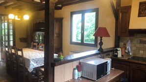Une cuisine équipée d’un four à micro-ondes, d’une table avec des chaises, de poutres en bois, d’une fenêtre et d’une lampe.