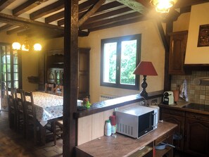 Eine Küche mit Mikrowelle, einem Tisch mit Stühlen, Holzbalken, einem Fenster und einer Lampe.