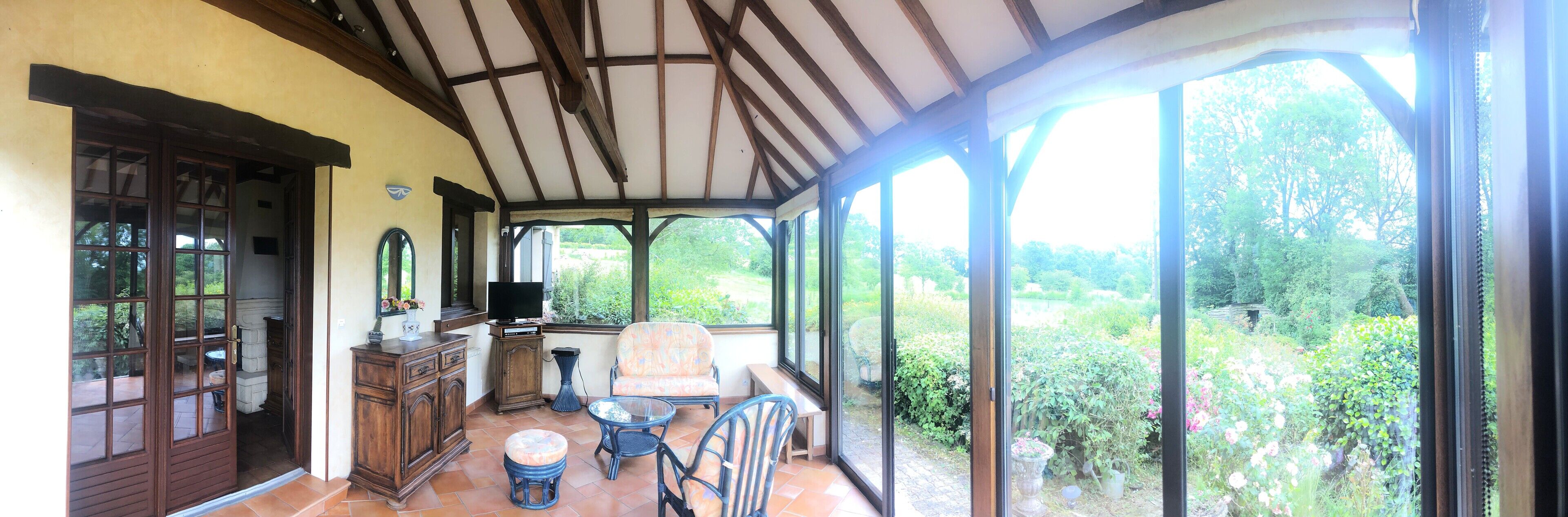 Une terrasse couverte avec un plafond en bois, un téléviseur et une vue sur un jardin.