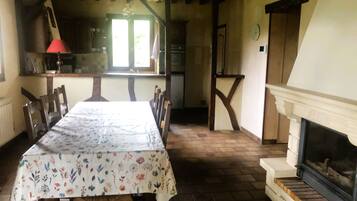 A dining room with a table set for six, wooden chairs, a fireplace, and a kitchen in the background.