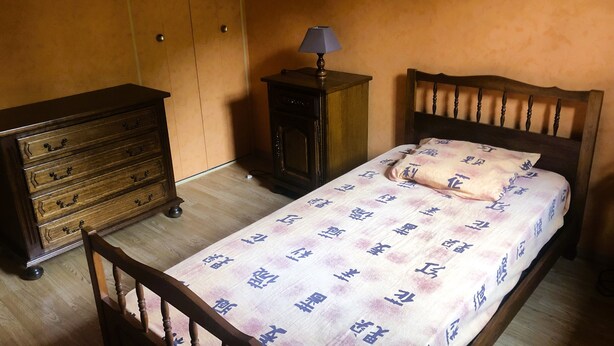 Une chambre à coucher avec un lit en bois, une table de chevet avec une lampe, une commode et une armoire.