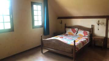 A bedroom with a wooden bed, a nightstand, a window with curtains, and a wall-mounted light fixture.