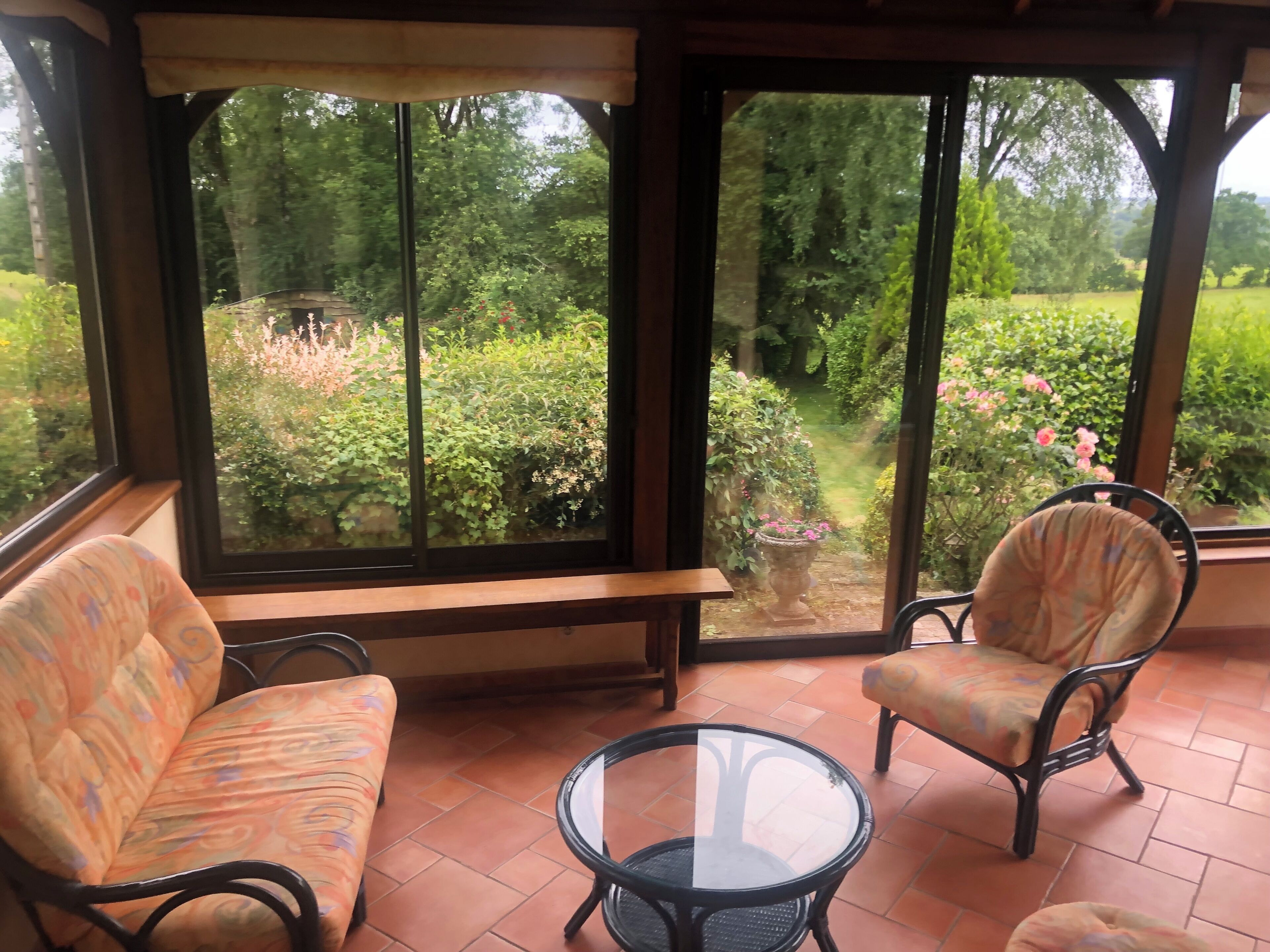 A room with a large window, a bench, two chairs, and a small table.