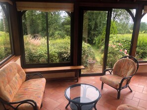 Una habitación con un ventanal grande, una banca, dos sillas y una pequeña mesa.