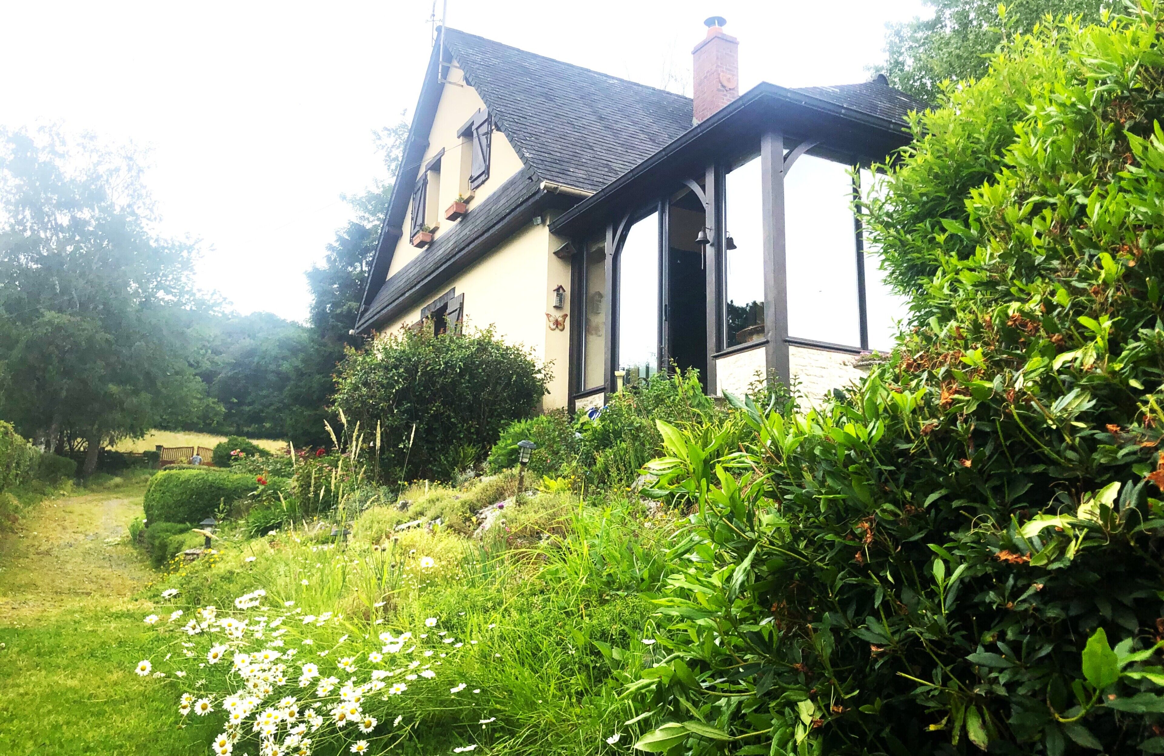 A traditional house with a sloped roof, surrounded by lush greenery and a garden with various plants and flowers.