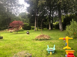 Eine begrünte Freifläche mit Bäumen, einem kleinen Busch und Spielzeug für Kinder.